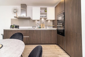 Een moderne keuken met houten kastjes, een inbouwoven en een eethoek met een marmeren tafel.