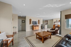 A spacious living room with a wooden coffee table, a sofa, and a TV on a wooden cabinet. - Hibisca Tropical Residences - 6BR Private Retreat (Grote Berg)