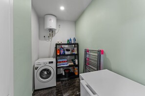 A laundry room with a washing machine, a dryer, a shelf with cleaning supplies, and a water heater. - Hibisca Tropical Residences - 6BR Private Retreat (Grote Berg)
