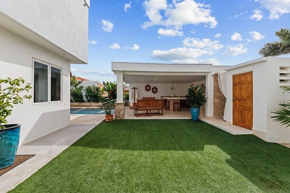 Een modern huis met een overdekt terras, een zwembad en een verzorgd gazon.