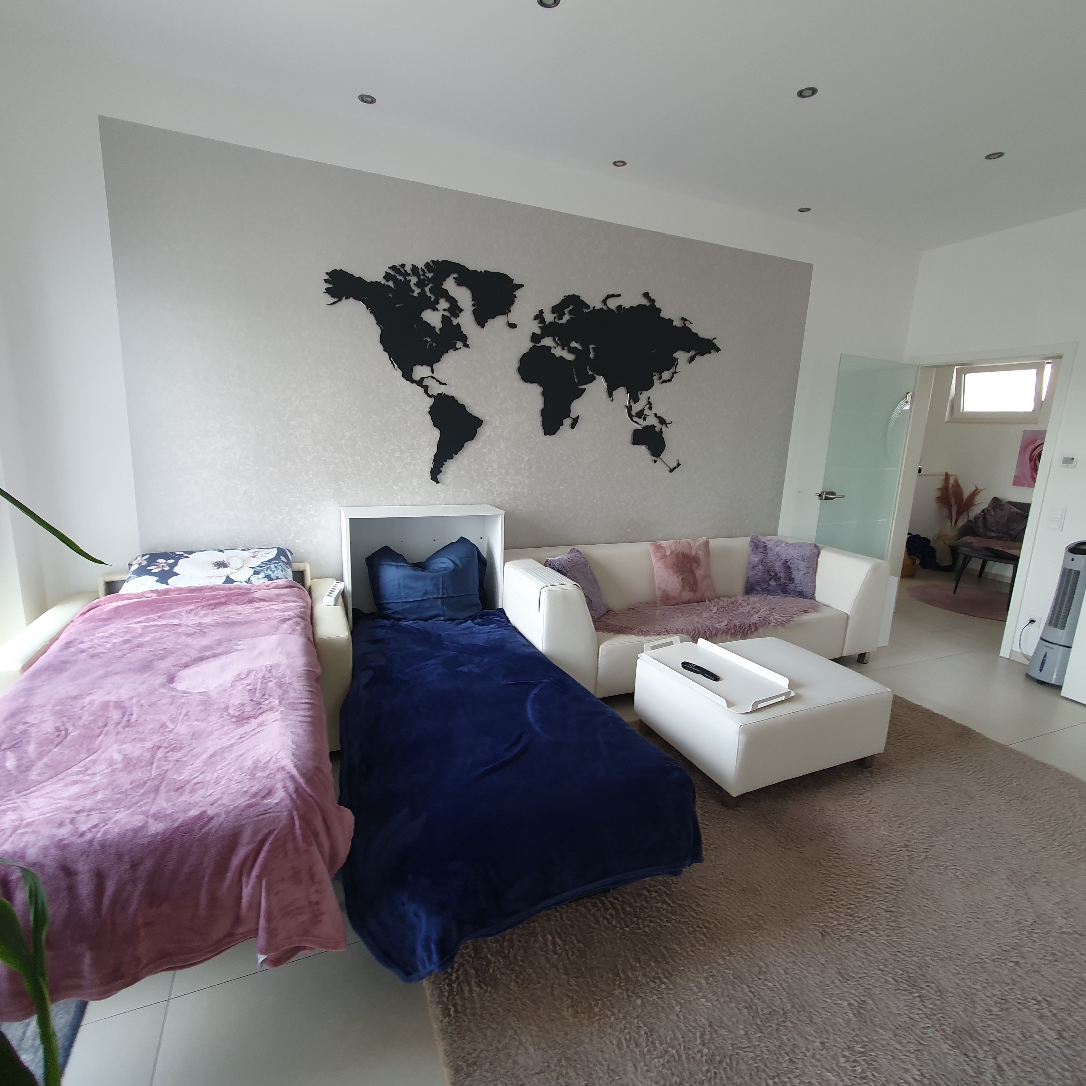 Ein modernes Schlafzimmer mit zwei Betten, einer Weltkarte an der Wand und Blick auf den angrenzenden Wohnbereich.