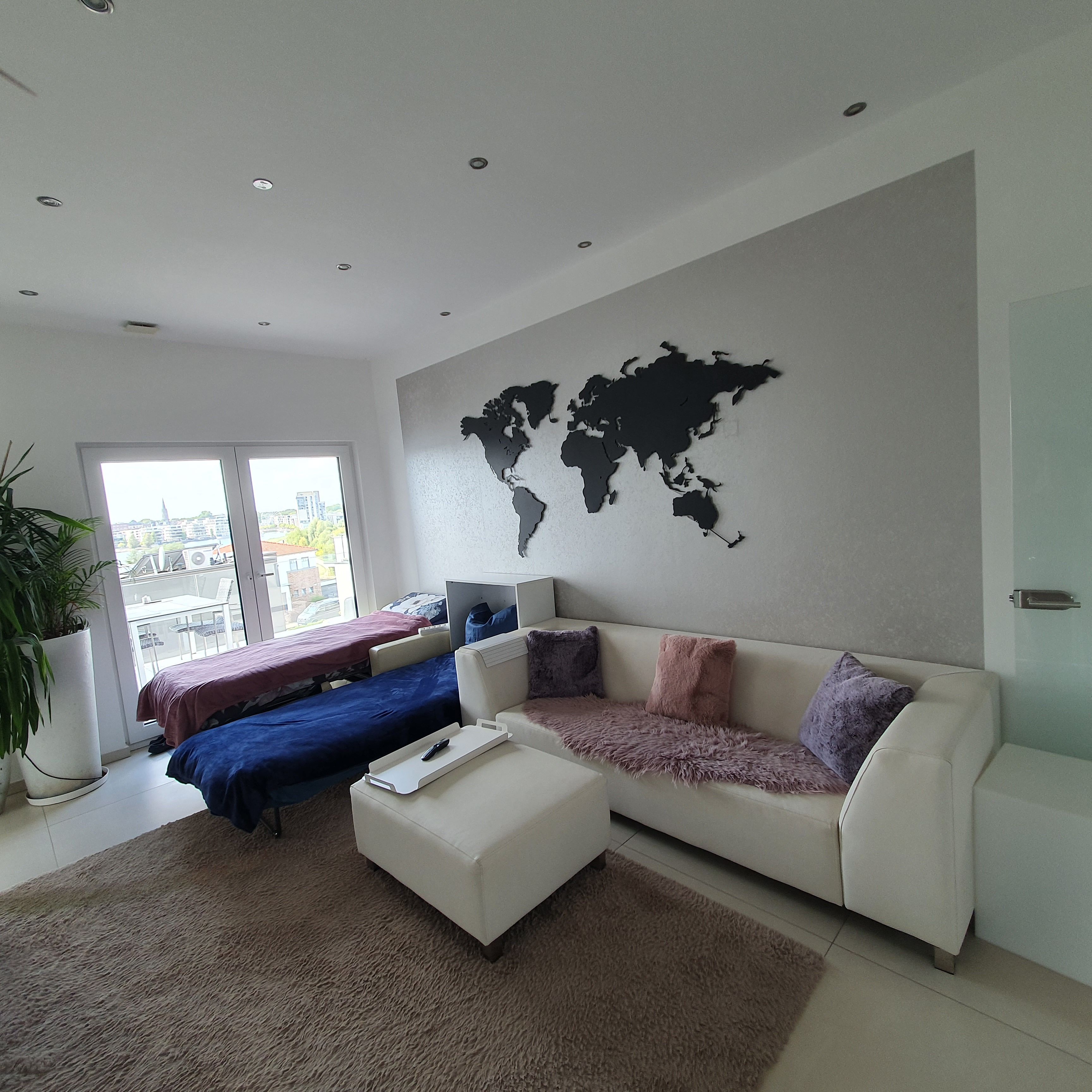 Un salon moderne agrémenté d’une décoration murale représentant une carte du monde, d’un canapé, d’une table basse et d’une grande fenêtre offrant une vue sur les bâtiments.