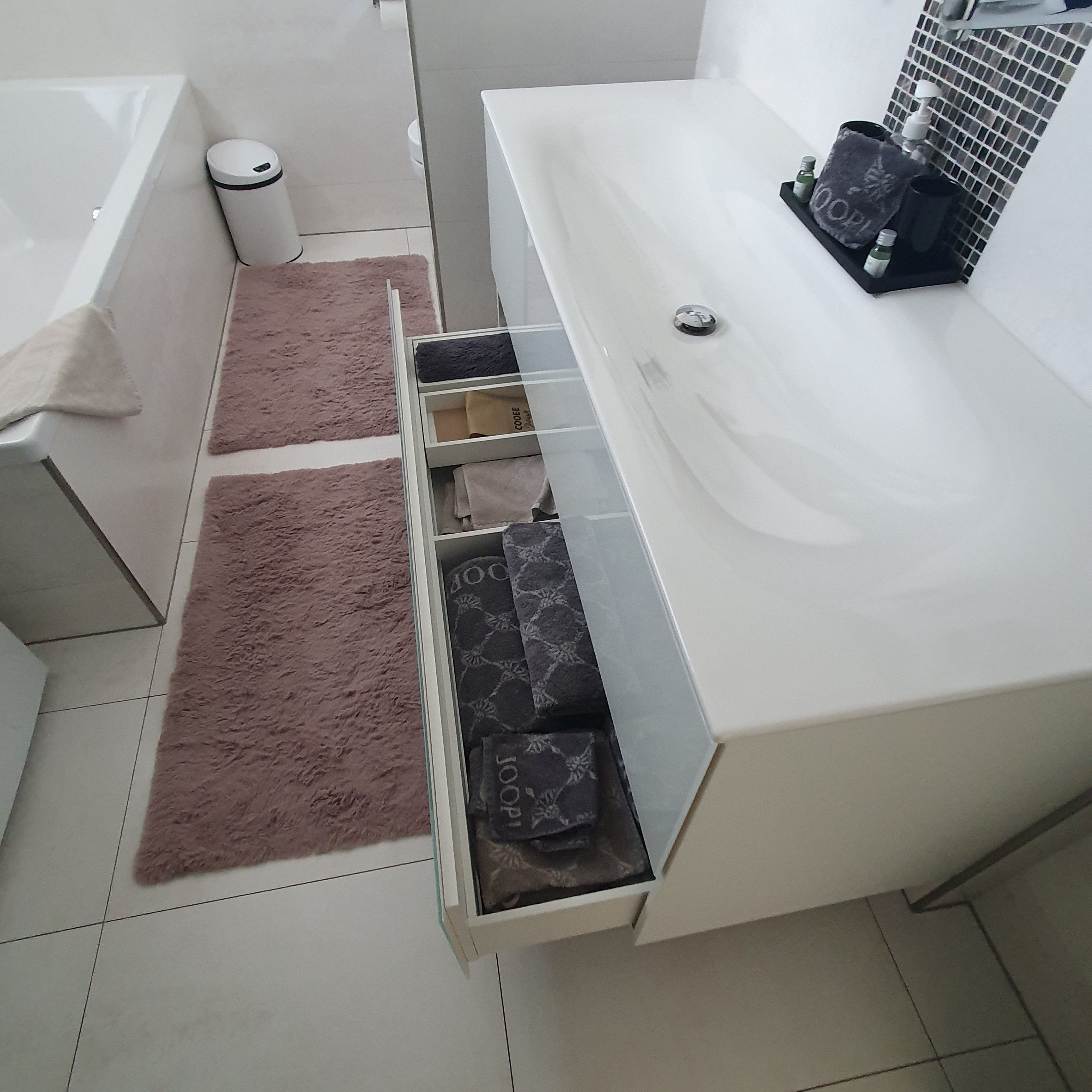 Ein Badezimmer mit einem weißen Waschbecken, einem Handtuchhalter, einem Mülleimer und einer Schublade mit gefalteten Handtüchern.