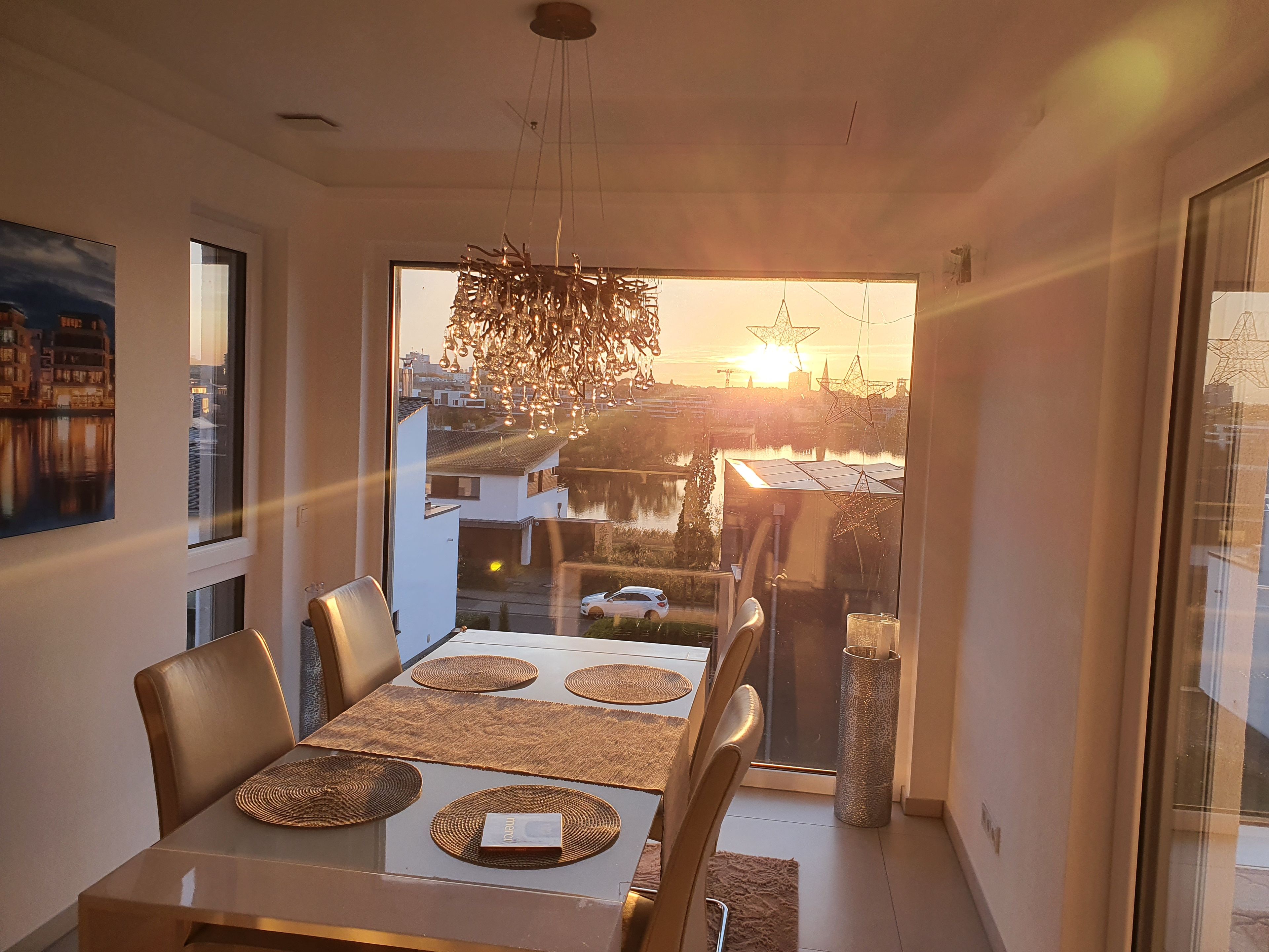 Een eetruimte met een tafel voor vier personen, een hanglamp en uitzicht op een stadslandschap door een groot raam.
