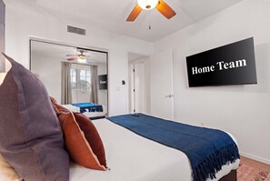 Ein Schlafzimmer mit einem Bett, einem Deckenventilator, einem Fernseher und einem Schild mit der Aufschrift 'Home Team' an der Wand.