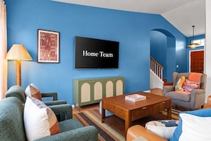 Ein Wohnzimmer mit blauen Wänden, einem Flachbildfernseher, einem grünen Schrank und einer Treppe.