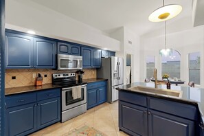 A modern kitchen with blue cabinets, stainless steel appliances, and a large island with a sink. - The Sunny Social | Pool • Hot Tub • Games Galore! (Chandler)
