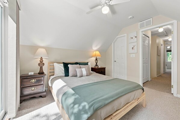 A bedroom with a bed, bedside lamps, a nightstand, a ceiling fan, and a door leading to another room. - Crawford Lake Winter Retreat (Kalkaska)