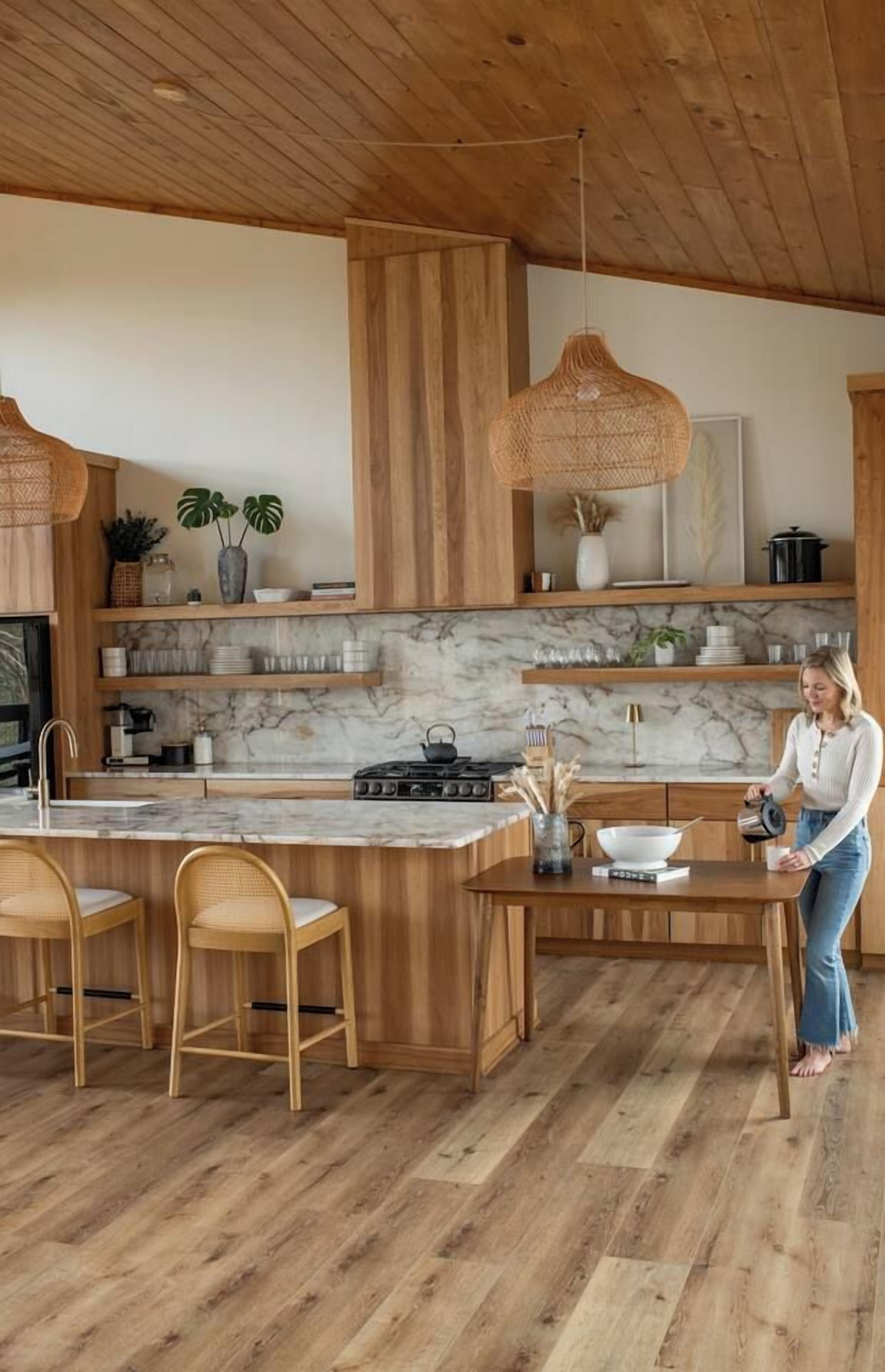 A modern kitchen with wooden cabinetry, a marble countertop, and a central island with bar stools.