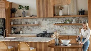 A modern kitchen with wooden cabinetry, a marble countertop, and a central island with bar stools.