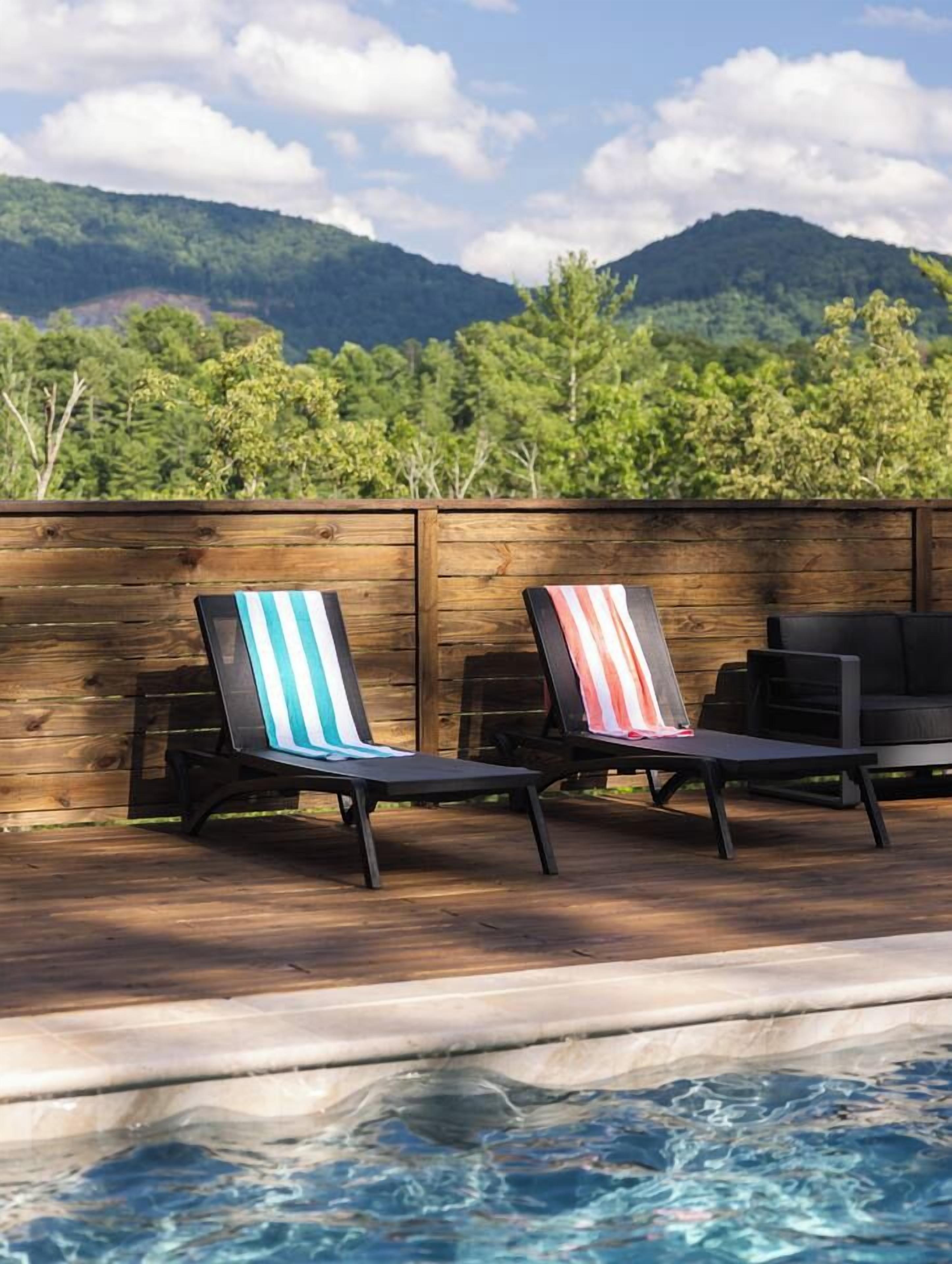 Área da piscina com duas espreguiçadeiras e cerca de madeira.