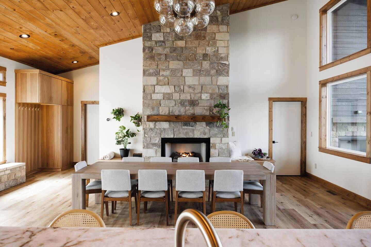A spacious dining area with a stone fireplace, wooden ceiling, and large windows.