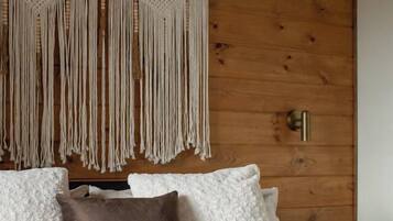 Uma cama com travesseiros brancos e castanhos, um pendente de macramé na parede e uma parede de madeira.