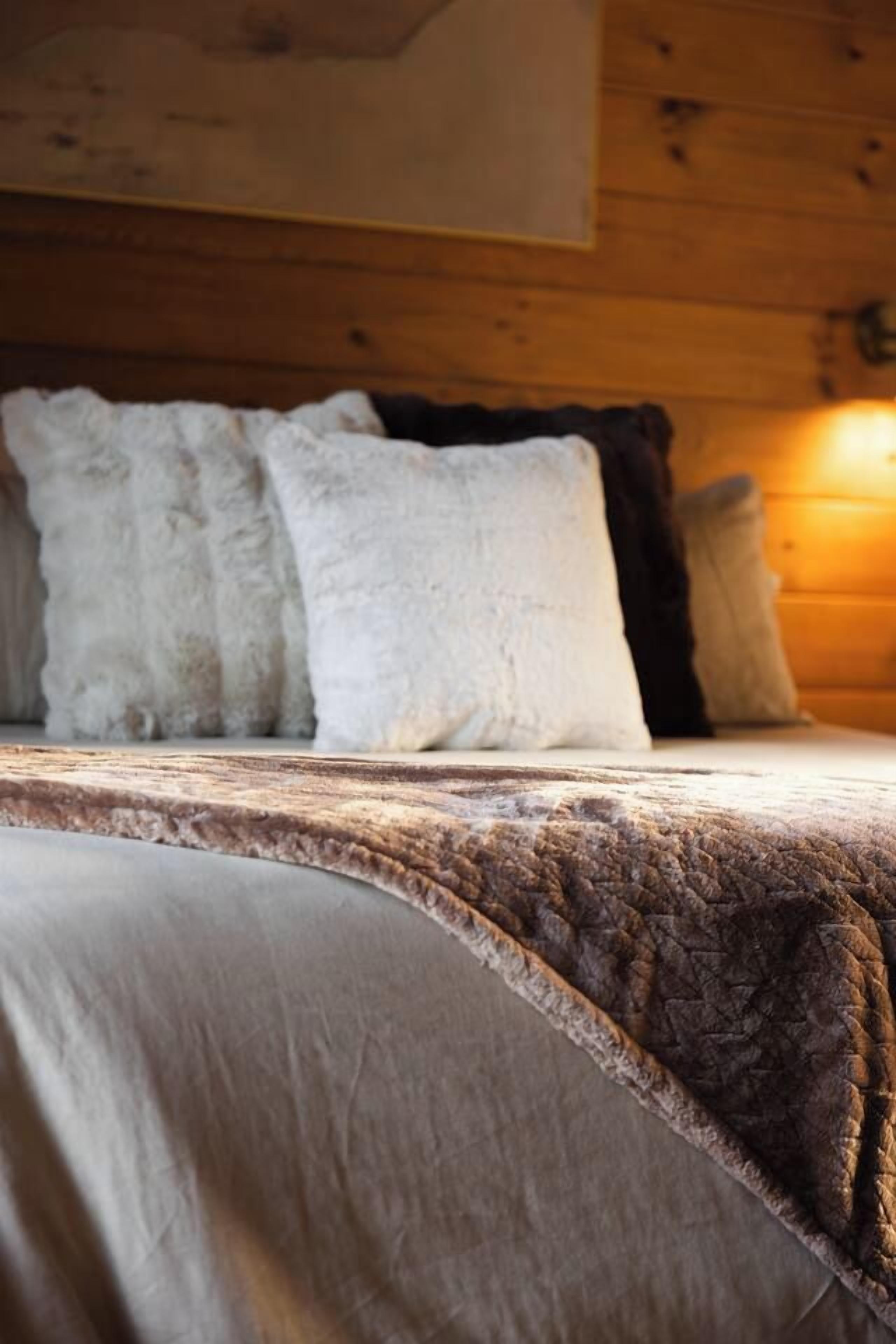 A bed with a textured blanket and pillows, a wooden headboard, and a wall-mounted light fixture.
