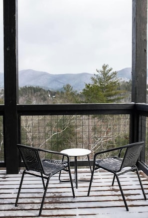 A wooden deck with two chairs and a table, overlooking a mountainous landscape.