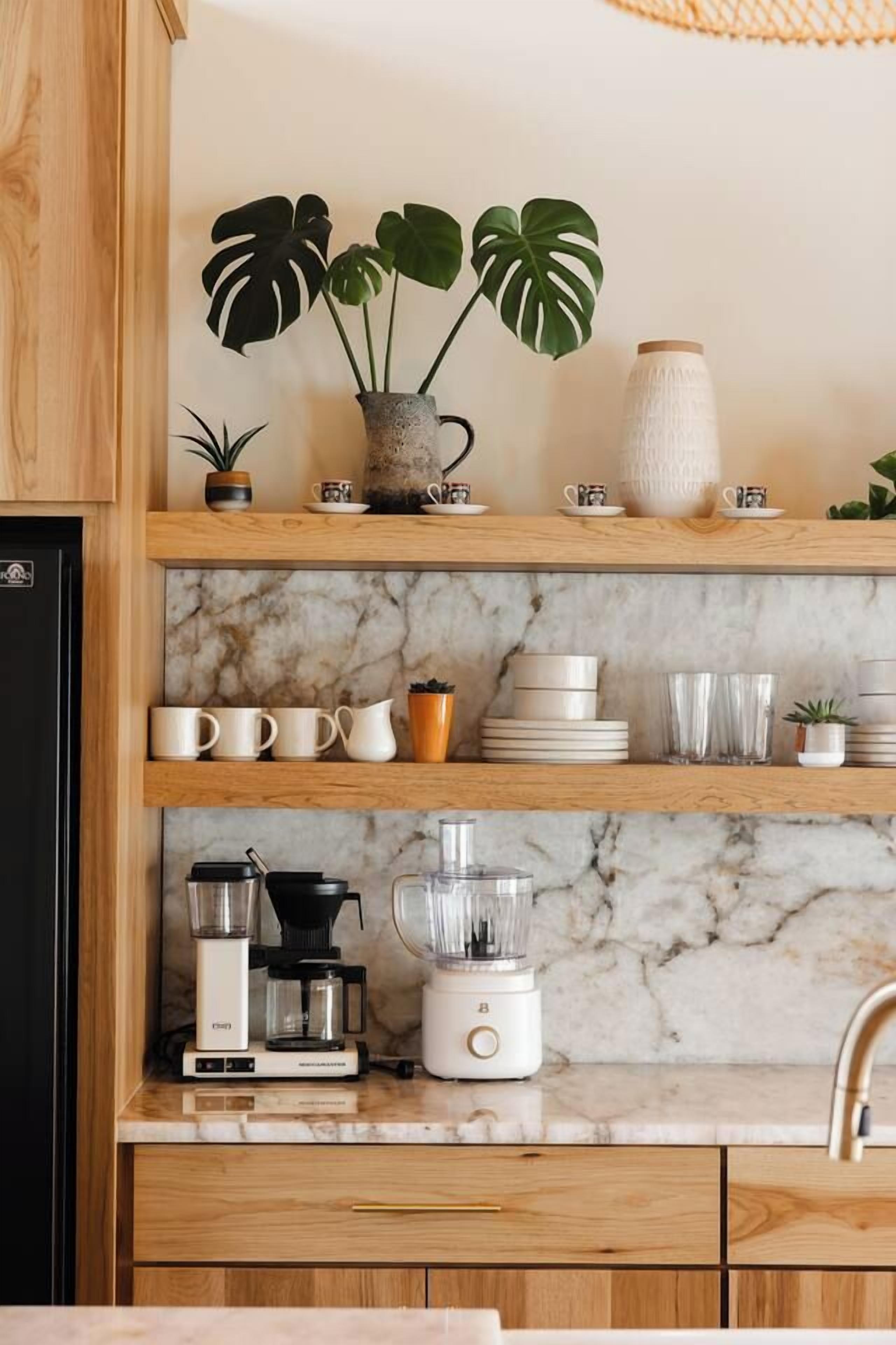 Una cocina con estantes de madera, encimera de mármol y varios electrodomésticos.