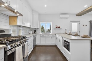 A modern kitchen with white cabinetry, a built-in oven, and a window providing a view of trees.