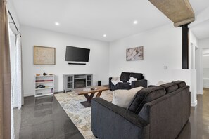 A modern living room with a grey sofa, a flat-screen TV, a fireplace, and a bookshelf.