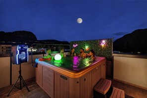 Un jacuzzi avec un panneau lumineux au néon et un projecteur sur trépied, sur un balcon, la nuit.