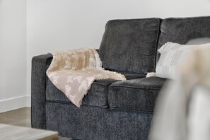 Um sofá cinzento com uma manta estampada e um travesseiro branco.