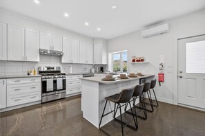 A modern kitchen with white cabinetry, stainless steel appliances, and a central island with bar stools.