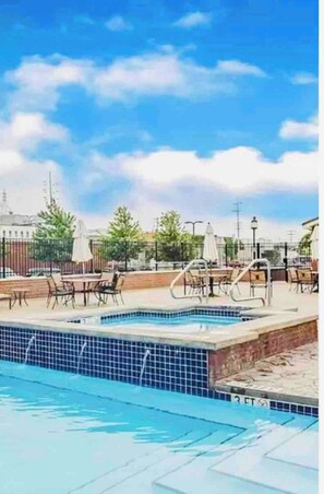 Ein Swimmingpool mit Liegestühlen und Sonnenschirmen, umgeben von einem Zaun und Bäumen.