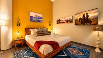 A bedroom with a wooden bed, a blue patterned rug, and wall art depicting landscapes and horses.