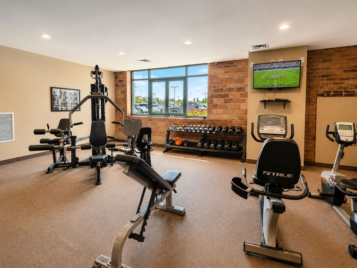 Een sportschool met diverse fitnessapparaten, een aan de muur bevestigde televisie en een raam met uitzicht.