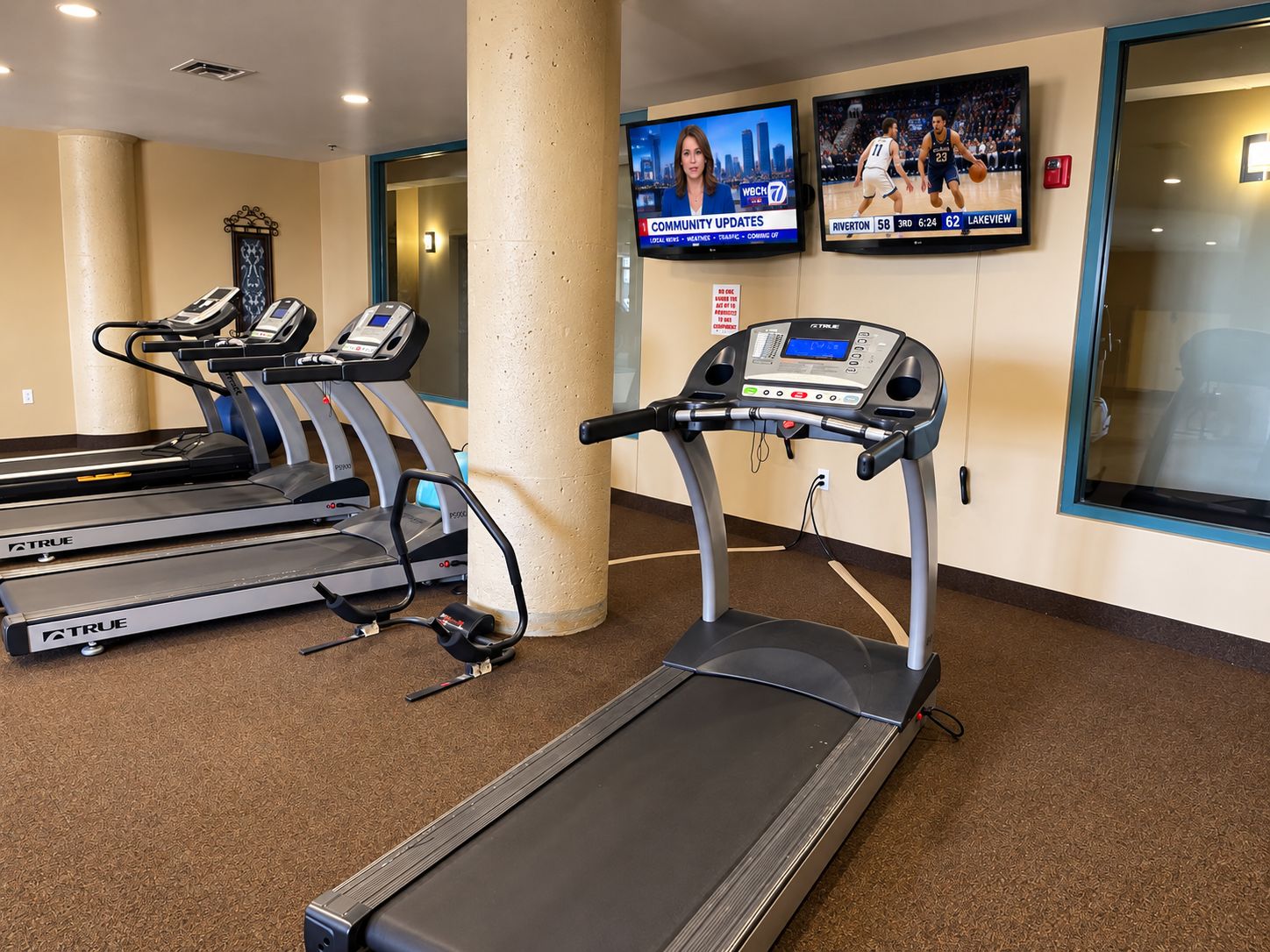 A gym with treadmills, a stationary bike, and a wall-mounted TV displaying sports.