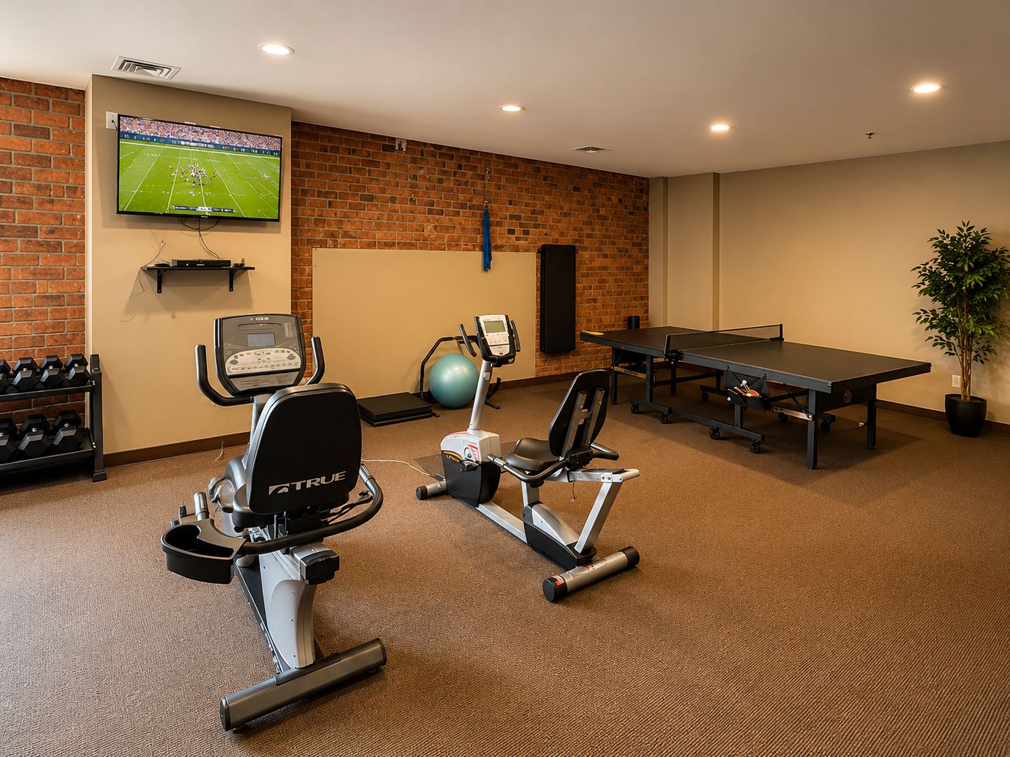 Een fitnessruimte met trainingsapparatuur, een televisie en een tafel.