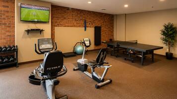 Een fitnessruimte met trainingsapparatuur, een televisie en een tafel.