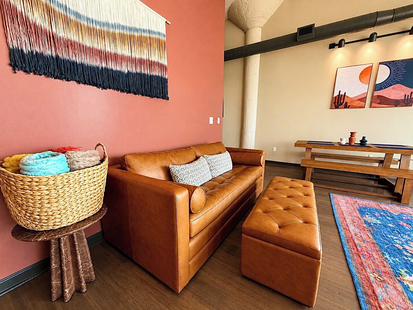A cozy living room with a brown leather sofa, a matching ottoman, a woven basket on a small table, and a colorful rug.