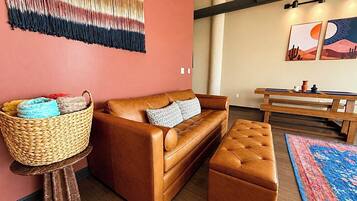 A cozy living room with a brown leather sofa, a matching ottoman, a woven basket on a small table, and a colorful rug.