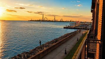 A waterfront promenade with a view of a distant roller coaster and a body of water reflecting the sunset.
