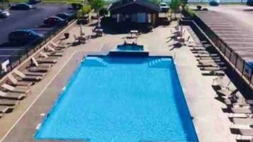 Une piscine avec un petit bâtiment au centre, entourée de chaises longues et d’une clôture.