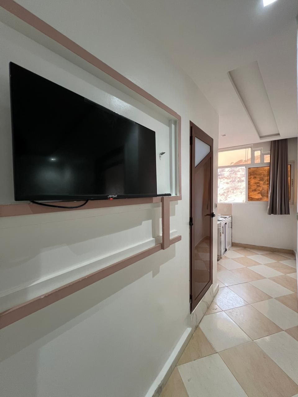 A room with a mounted flat-screen TV, a door, and a window with curtains.