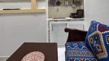 A compact living space with a television mounted on a wall, a dining table with a decorative plate, and a patterned sofa.
