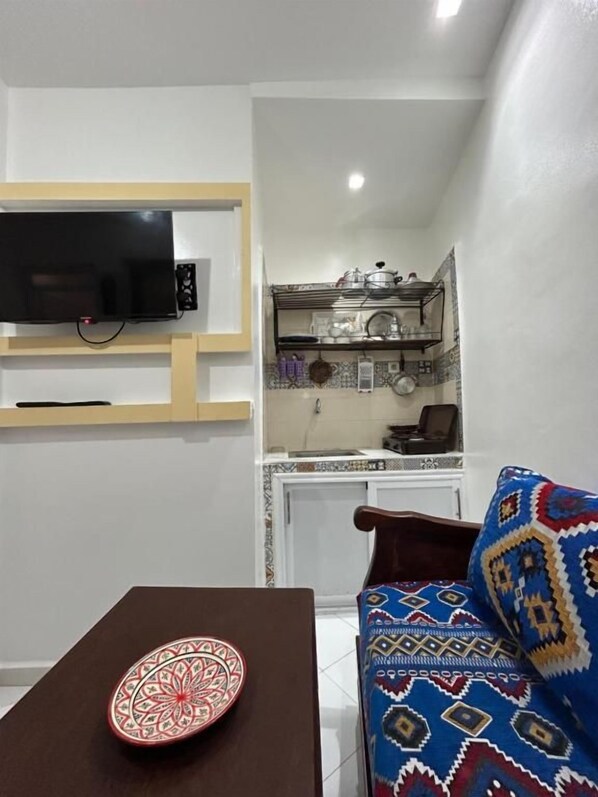 Un espace de vie compact avec un téléviseur fixé au mur, une table à manger agrémentée d’une assiette décorative et un canapé à motifs.