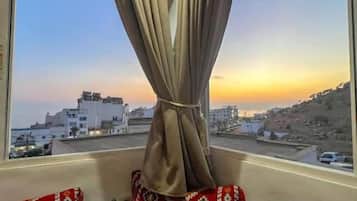 Habitación con vista a un paisaje urbano a través de una ventana con cortinas. Hay cojines estampados en un sofá.