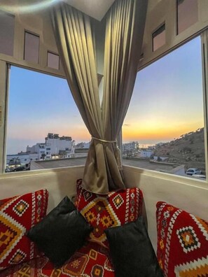 A room with a view of a cityscape through a window with curtains. There are patterned cushions on a sofa.