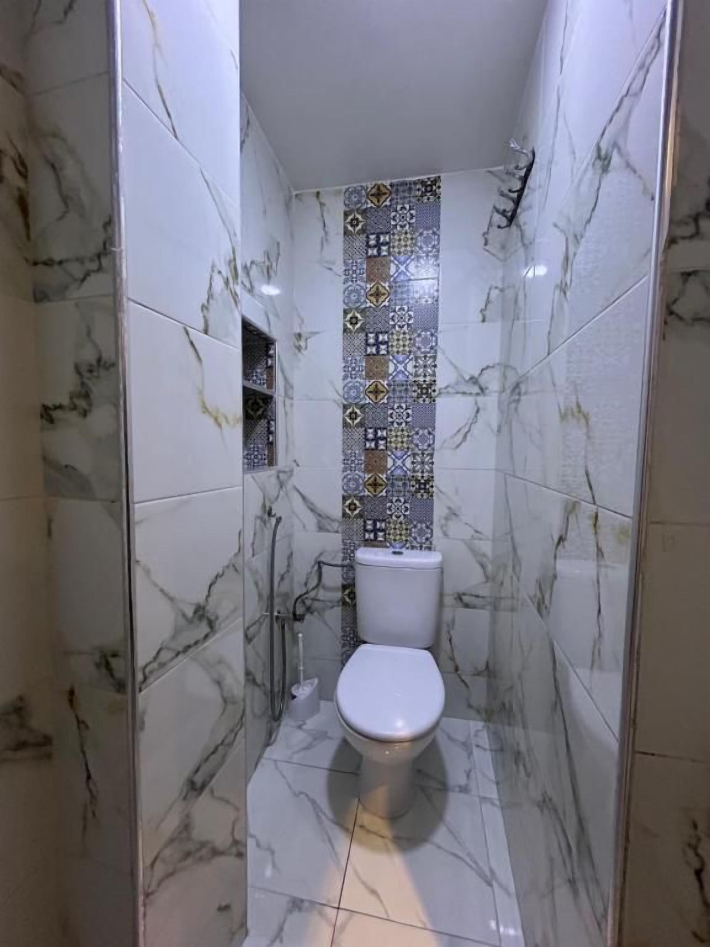 Ein Badezimmer mit weißer Toilette, einer Duschkabine und einer gefliesten Wand mit geometrischem Muster.