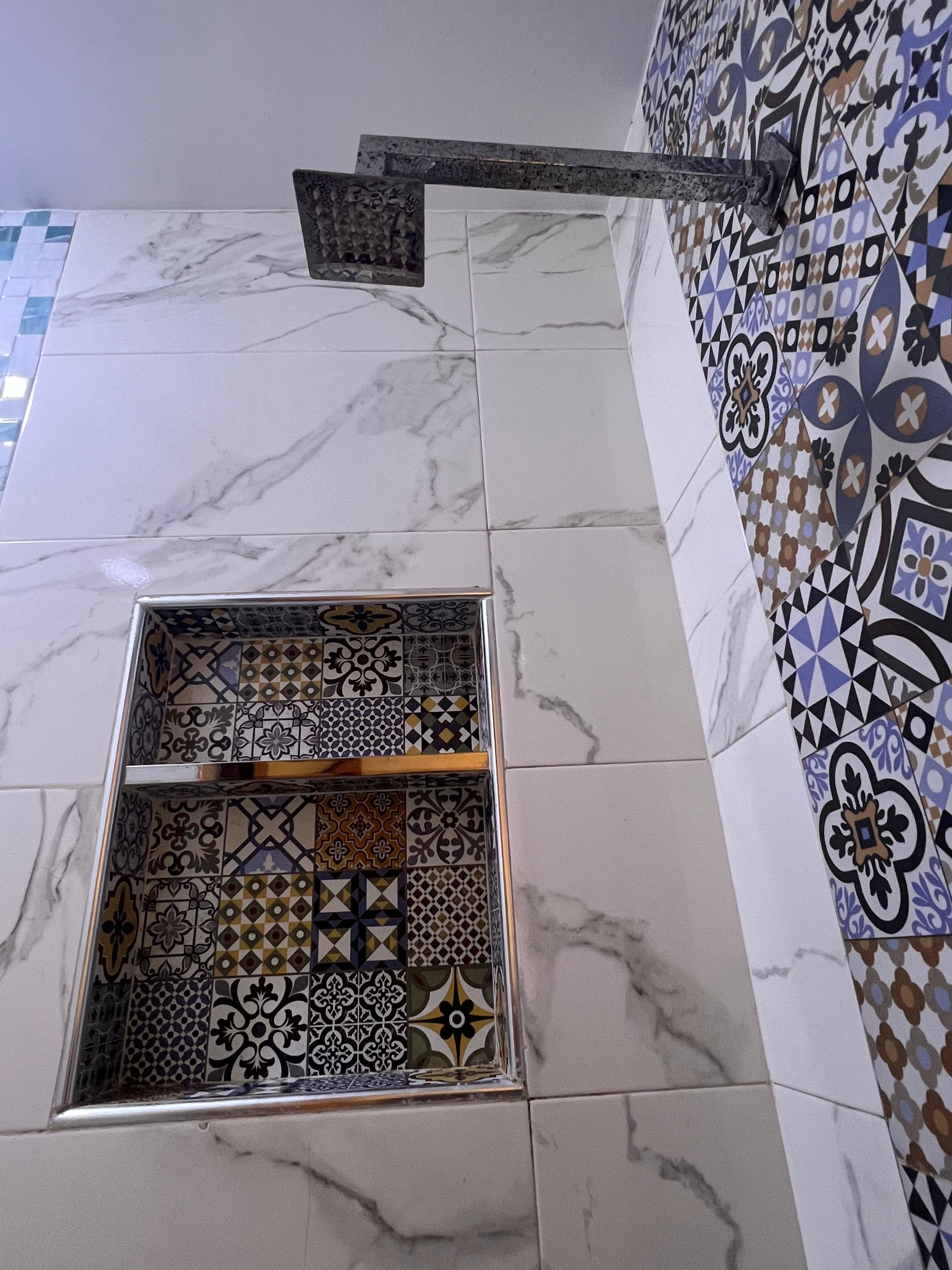 Un baño con piso de mármol, zona de ducha con azulejos y un diseño decorativo en la pared.