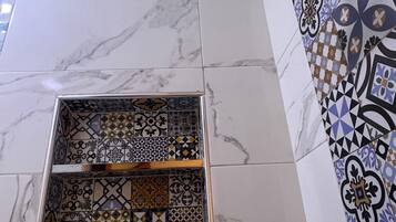 Un baño con piso de mármol, zona de ducha con azulejos y un diseño decorativo en la pared.