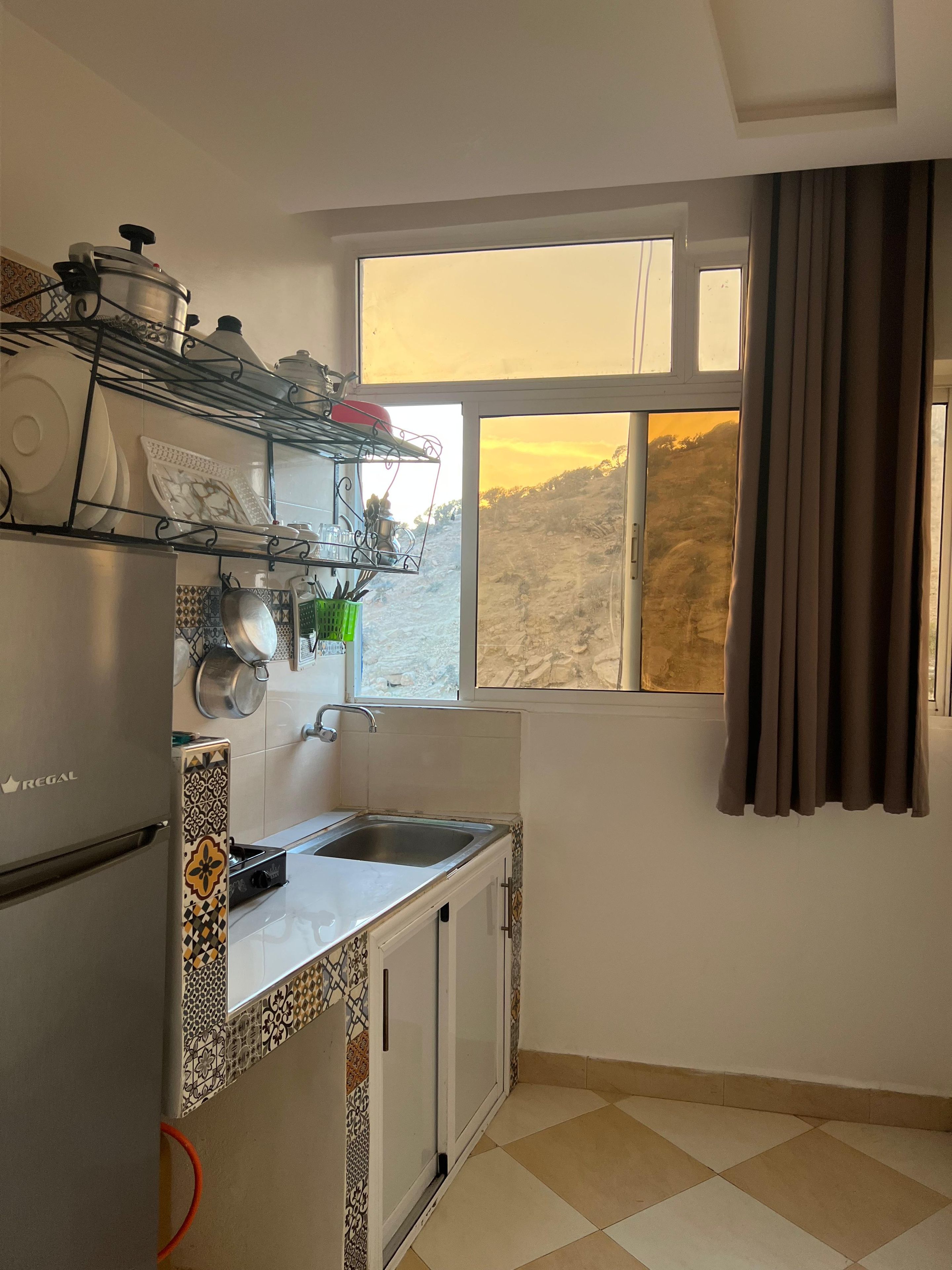 Cozinha equipada com frigorífico, pia e janela com cortinas.