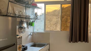 Cozinha equipada com frigorífico, pia e janela com cortinas.