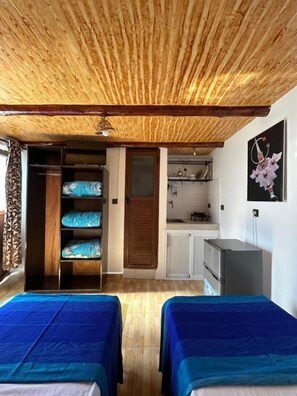 A room with two beds, a kitchenette, and a wooden ceiling.