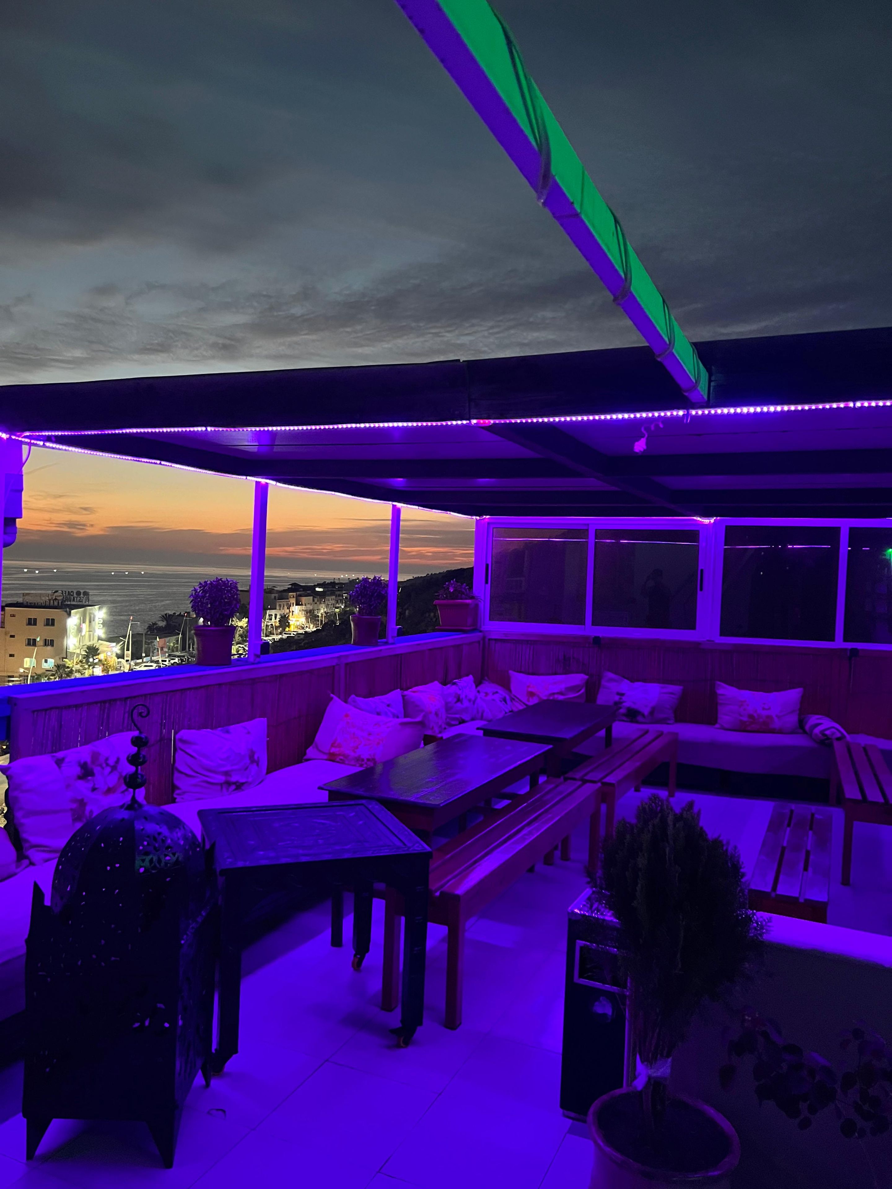 Terraza en la azotea con asientos y mesas, con vista a un paisaje urbano al anochecer.
