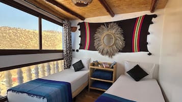 Quarto com duas camas, um tapete de parede tecido e vista para paisagem desértica.