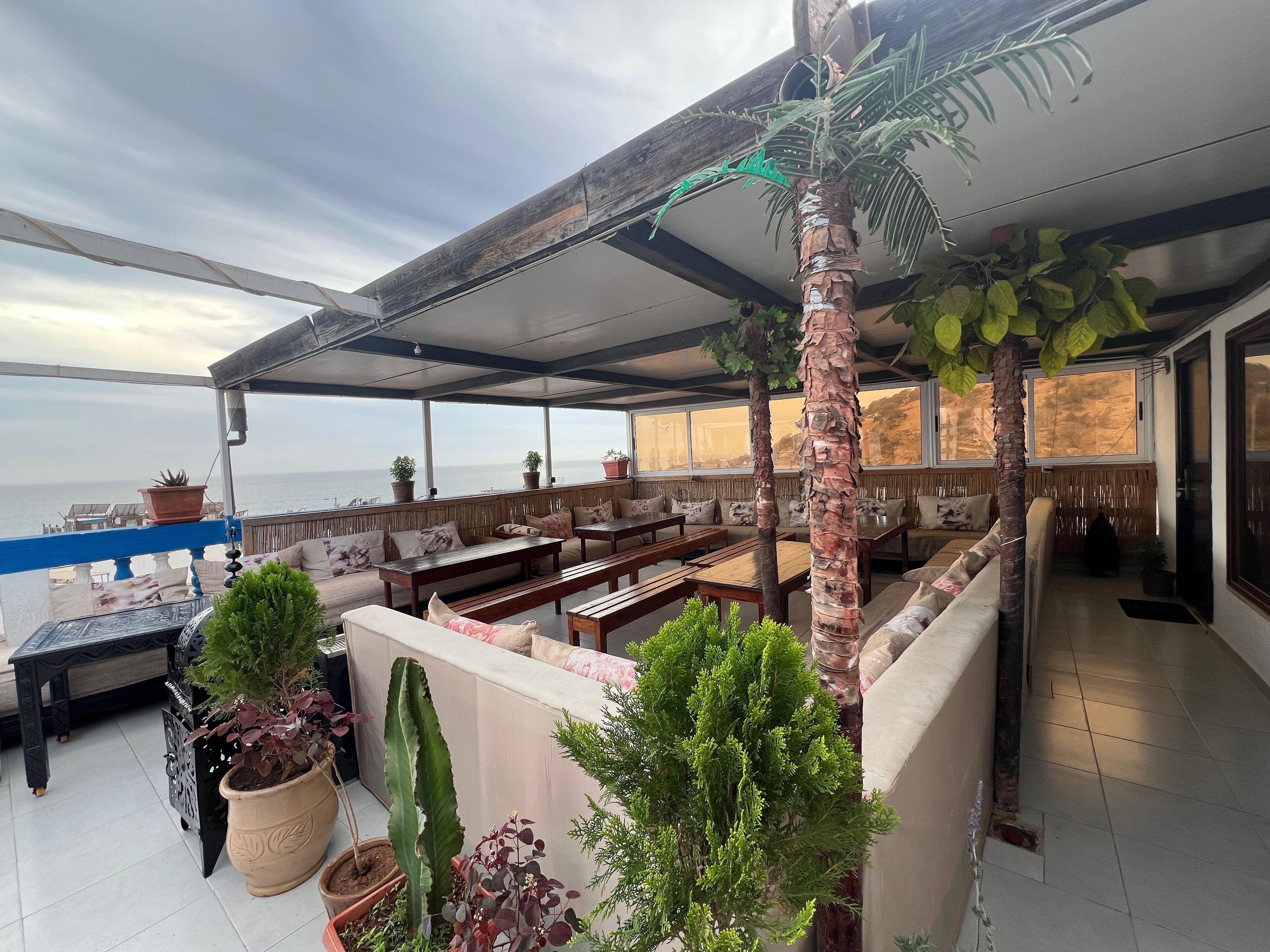 Un espace extérieur abrité, aménagé avec des tables et des chaises, des plantes en pot et offrant une vue sur la mer.