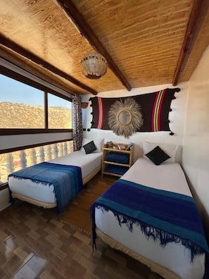 Een kamer met twee bedden, een houten plafond, een groot raam en een decoratief wandkleed.